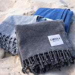 Ozoola Turkish beach towels in charcoal, blue and grey stonewash on sand