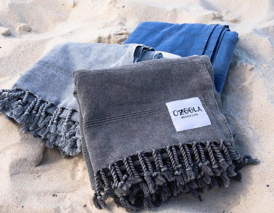 Ozoola Turkish beach towels in charcoal, blue and grey stonewash on sand
